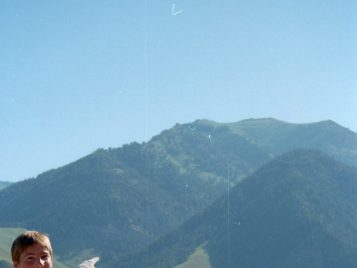 A female student holds a hand-made sign that says 134.50. She is pointing at a mountain.